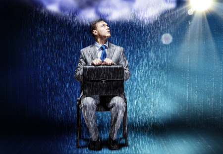 Young businessman under rain sitting on chainの写真素材