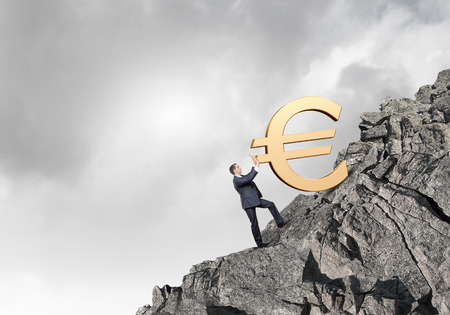 Businessman rolling euro sign up the hillの写真素材