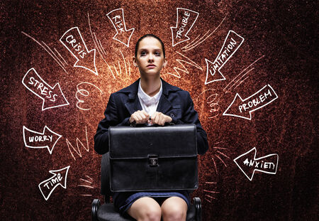Young upset businesswoman sitting on chair with briefcase in handsの写真素材