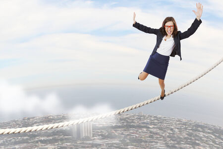 Young attractive businesswoman balancing on rope high in skyの写真素材