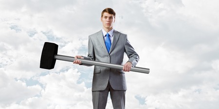 Young determined businessman with big hammer in handsの写真素材