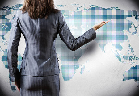 Rear view of businesswoman and world map at backgroundの写真素材