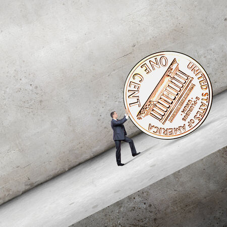 Businessman rolling cent coin up the hillの写真素材