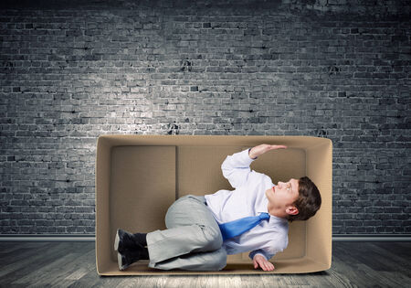 Young frustrated businessman trapped in small carton boxの写真素材