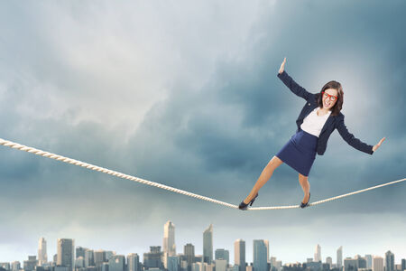 Young attractive businesswoman balancing on rope high in skyの写真素材