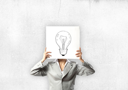Businesswoman hiding her face with sheet of paper with sketches at backgroundの写真素材