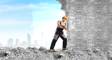 Strong man in uniform and helmet pushing wall  Place for textの写真素材