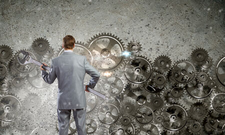 Rear view of determined businessman with wrench in hands and cogwheels at backgroundの写真素材