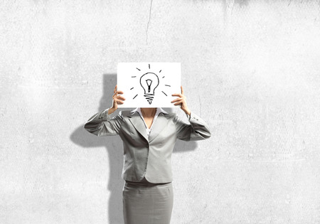 Businesswoman hiding her face with sheet of paper with sketches at backgroundの写真素材