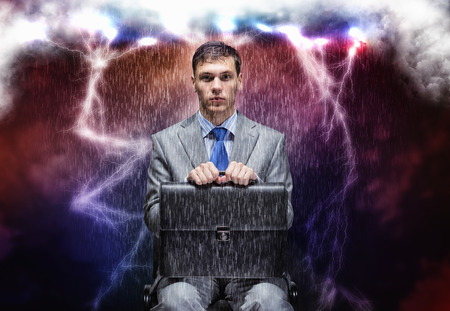 Young businessman under rain sitting on chainの写真素材
