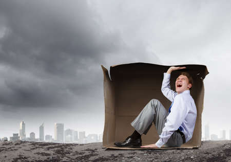 Young frustrated businessman trapped in small carton boxの写真素材