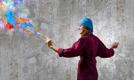 Young woman painter with brush and colorful splashes aboveの写真素材