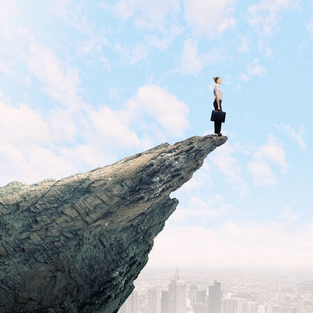 Risky businesswoman standing on edge of rockの写真素材