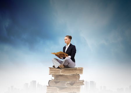 Young attractive businesswoman sitting on pile of old books readingの写真素材