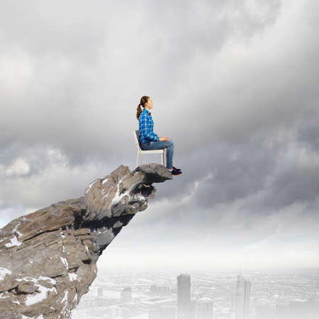 Young woman in shirt sitting in chair on rock topの写真素材