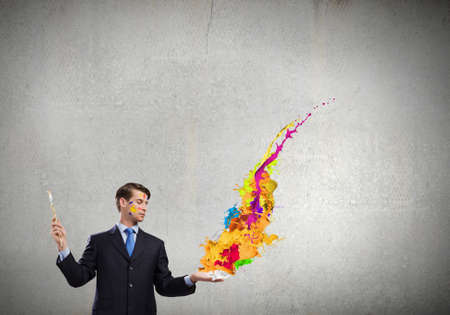 Young businessman with brush in hand and colorful paint splashesの写真素材