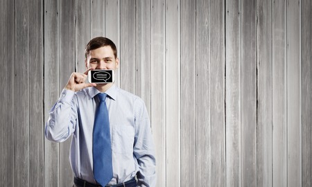 Young handsome businessman hiding mouth behind mobile phoneの写真素材