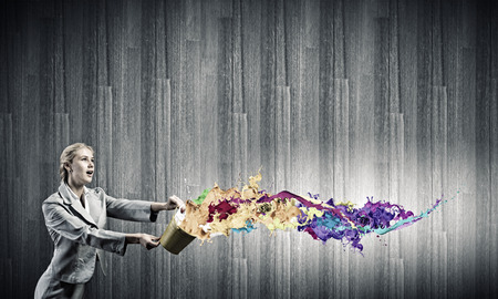 Young businesswoman holding bucket with paint splashesの写真素材