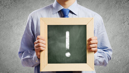 Young smiling businessman holding chalkboard with exclamation signの写真素材