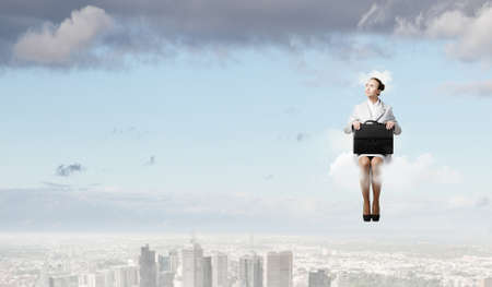 Young pretty businesswoman sitting on cloud high above cityの写真素材