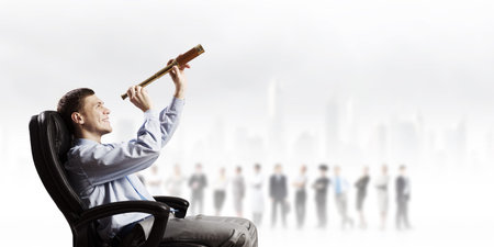 Young businessman in chair looking in to spyglass