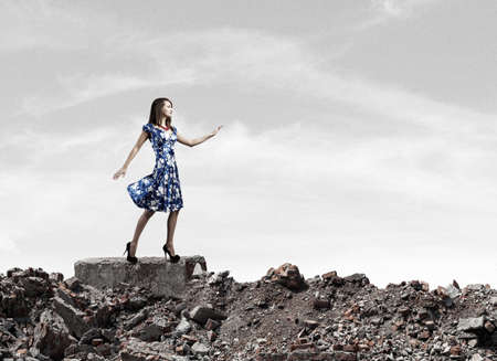 Young woman in blue dress walking among city ruinsの写真素材