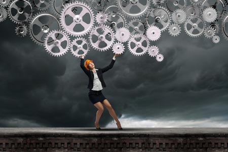 Young woman engineer holding mechanism of cogwheels above headの写真素材
