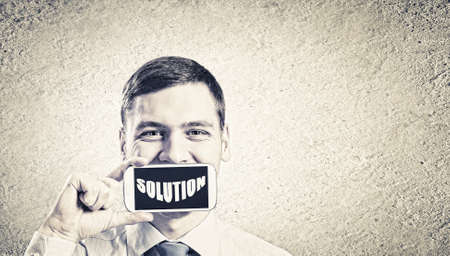 Young handsome businessman hiding mouth behind mobile phoneの写真素材