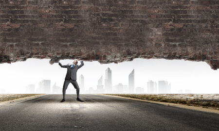 Young powerful businessman lifting brick wall above headの写真素材