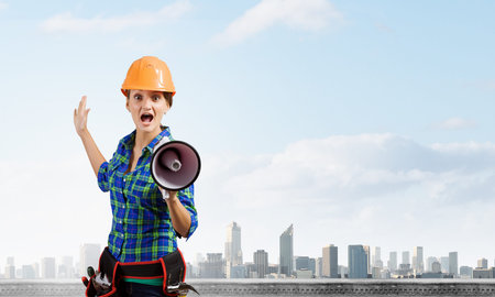 Young woman builder in hardhat screaming in megaphoneの写真素材
