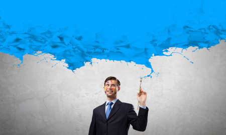 Young businessman with brush in hand and paint splashesの写真素材