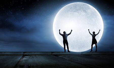 Silhouettes of young romantic couple standing under the moon lightの写真素材