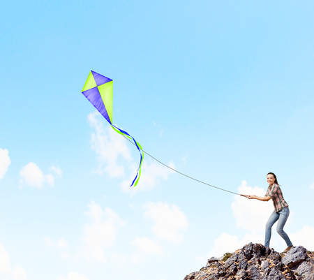 Young pretty woman standing on rock with colorful kiteの写真素材