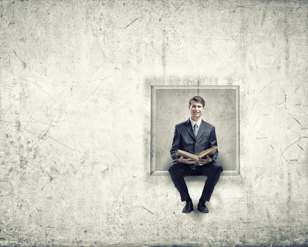 Young businessman sitting in cube with bookの写真素材