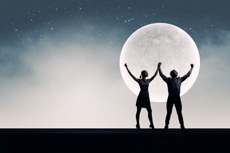 Silhouettes of young romantic couple standing under the moon lightの写真素材