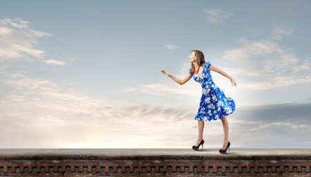 Young woman in blue dress walking on roof of buildingの写真素材