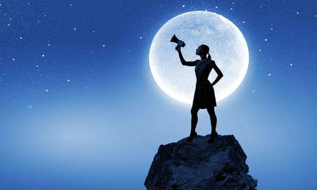 Young woman speaking in megaphone against full moonの写真素材