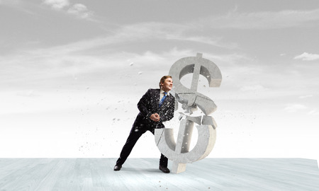 Young businessman breaking stone dollar sign. Currency conceptの写真素材