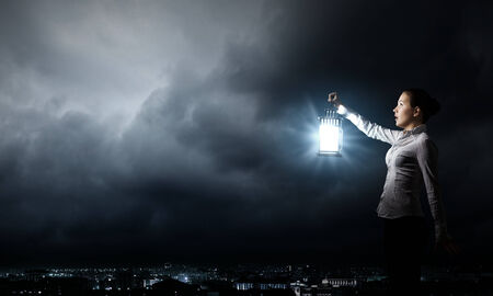 Young pretty businesswoman with lantern in darknessの写真素材