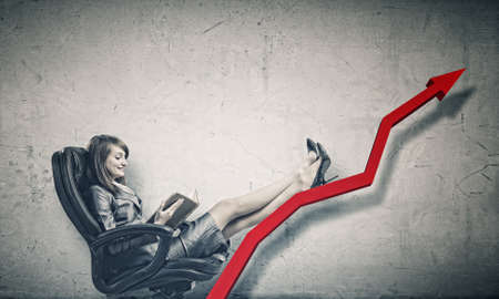 Young attractive businesswoman sitting in chair and reading bookの写真素材