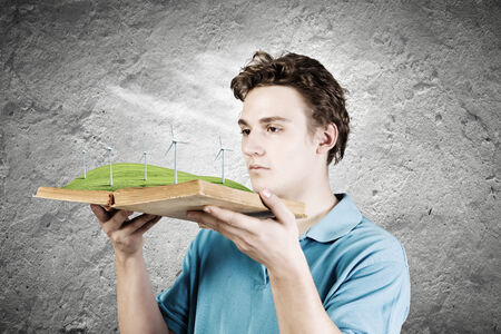 Young man in casual holding opened book with windmillsの写真素材