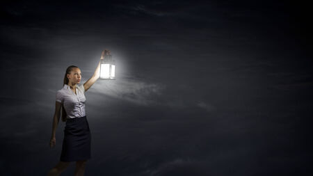 Young businesswoman walking in darkness with lantern in handの写真素材