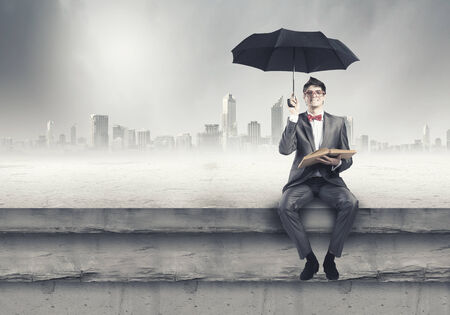 Young man in suit sitting on bench with book in handsの写真素材