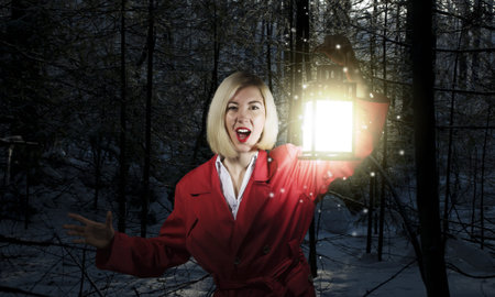 Young blonde in red cloak with lantern in night forest