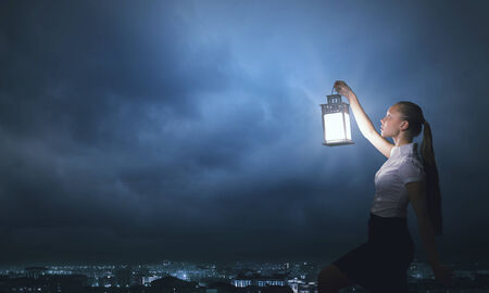 Young businesswoman walking in darkness with lantern in handの写真素材