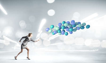 Young businesswoman running with bunch of colorful balloonsの写真素材