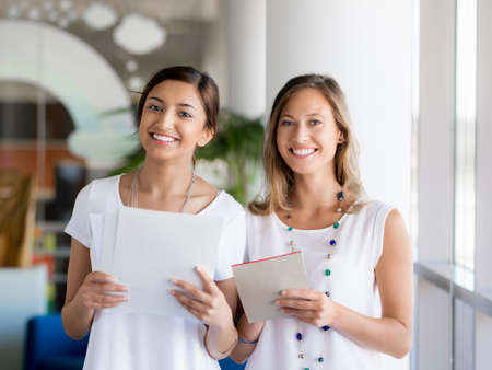 Two female collegues standing next to each other in an officeの写真素材