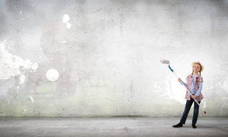 Cute girl of school age painting wall with rollerの写真素材