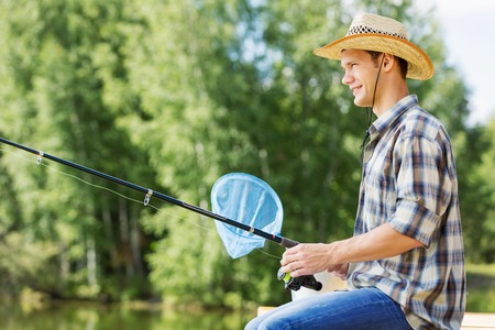 Young guy in hat sitting on bridge and fishingの写真素材