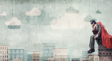 Young man in superhero costume sitting on top of buildingの写真素材